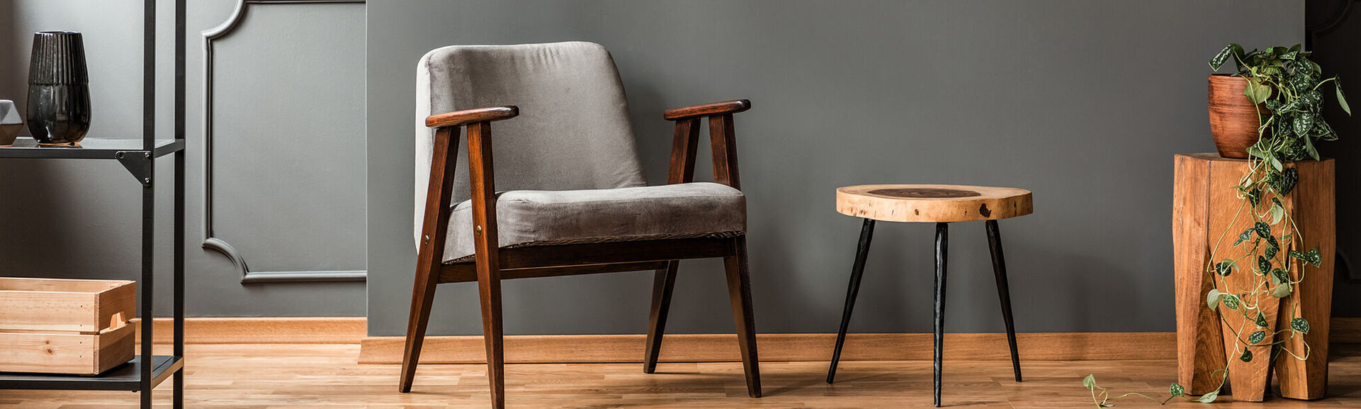 Grey armchair next to a wooden table in living room interior with plant and poster