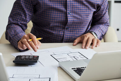Someone holding a calculator over a contract with a small house in the background