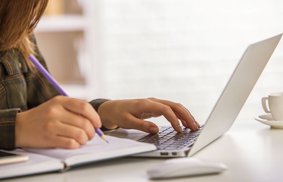 Someone writing in a notebook and typing on a computer