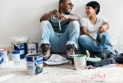 Two people sitting on the floor in front of paint cans