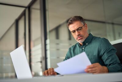 Someone looking at a sheet of paper in front of a laptop