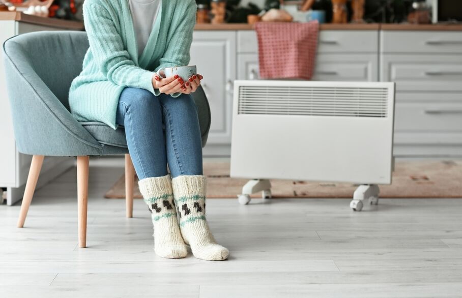 Someone in knitted socks with a mug sitting in front of a radiator