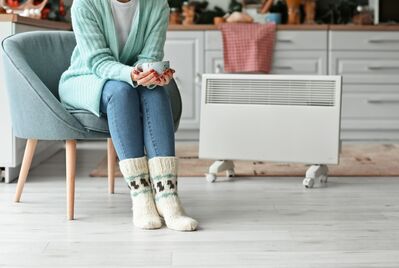 Someone in knitted socks with a mug sitting in front of a radiator