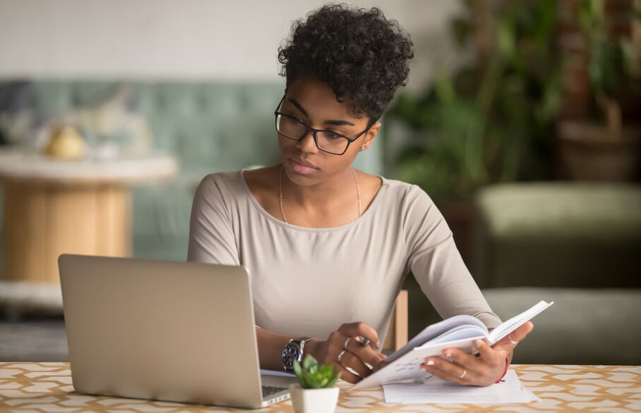 Someone looking at a laptop and holding a book