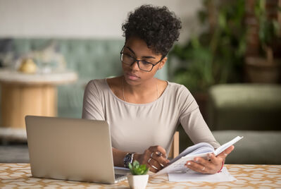 Someone looking at a laptop and holding a book