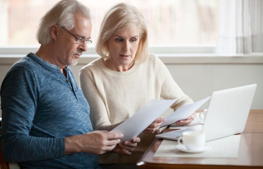 Two people looking at paper in front of a laptop