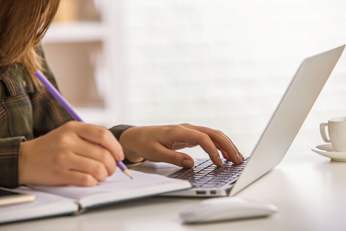 Someone writing in a notebook and typing on a computer