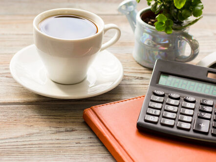 Close up of a calculator on a notebook, beside a cup of coffee