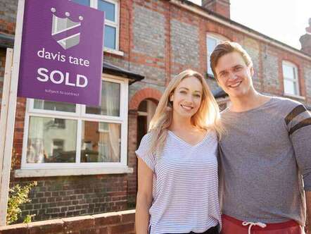 Two people standing in front of a house with a Davis Tate SOLD sign